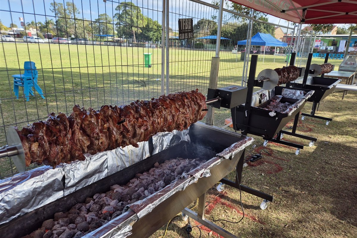 Multiple charcoal spit roasters cooking meat at a Brisbane community event